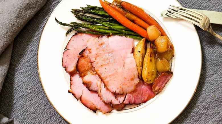 a plate of sliced Slow Cooker Easter Ham With Apricot And Kahlúa with asparagus, carrots, and onions on a gray tablecloth