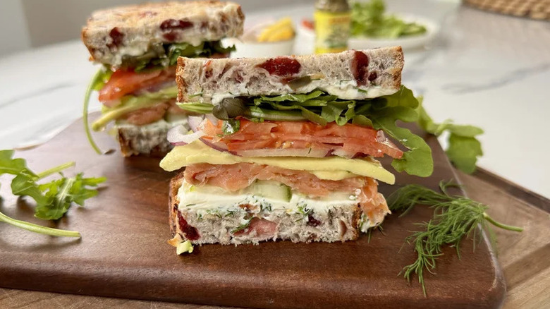 a halved Smoked Salmon Sandwich on a wooden cutting board with sprigs of fresh greens