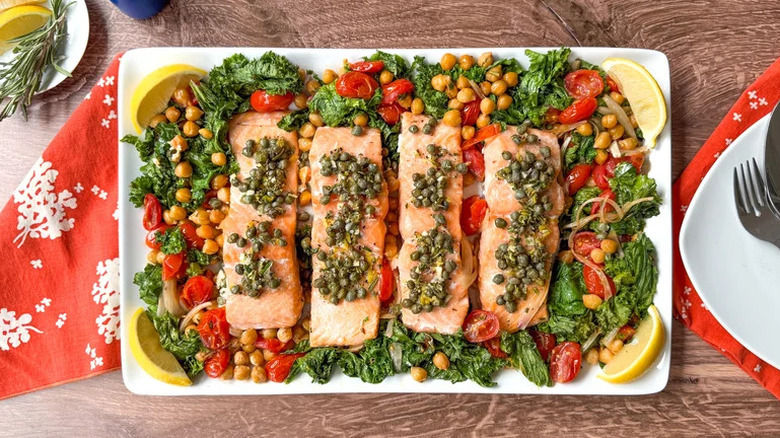 A tray with salmon, chickpeas, wilted greens, tomatoes, and lemon garnish