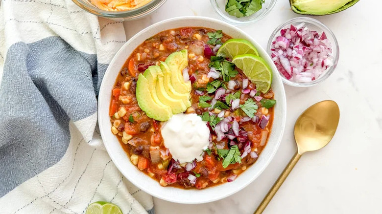 A bowl of vegetarian chili topped with avocado, cilantro, onion, lime, and other garnishes