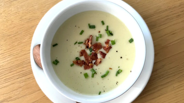A bowl of potato leek soup topped with crumbled bacon and scallions