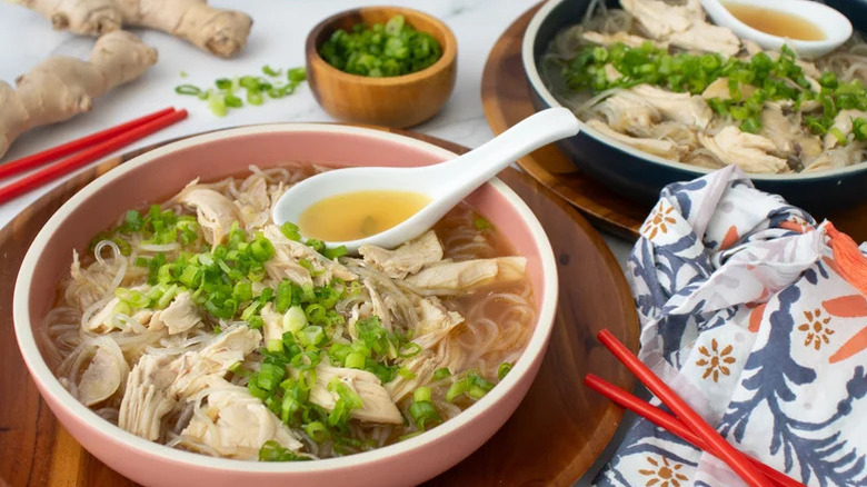 A bowl of soup with chicken, herbs, and rice noodles