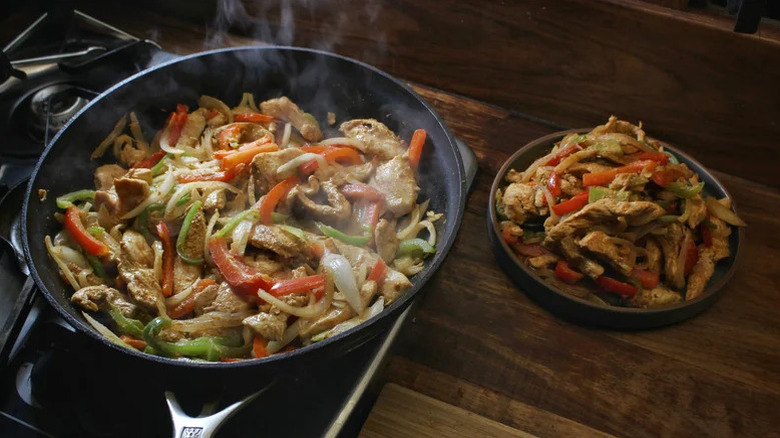 A skillet with chicken fajitas cooking, with a plate of prepared fajitas to the right
