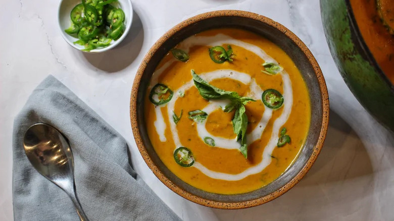 A bowl of pumpkin-coconut soup with a creamy swirl and scallion garnish