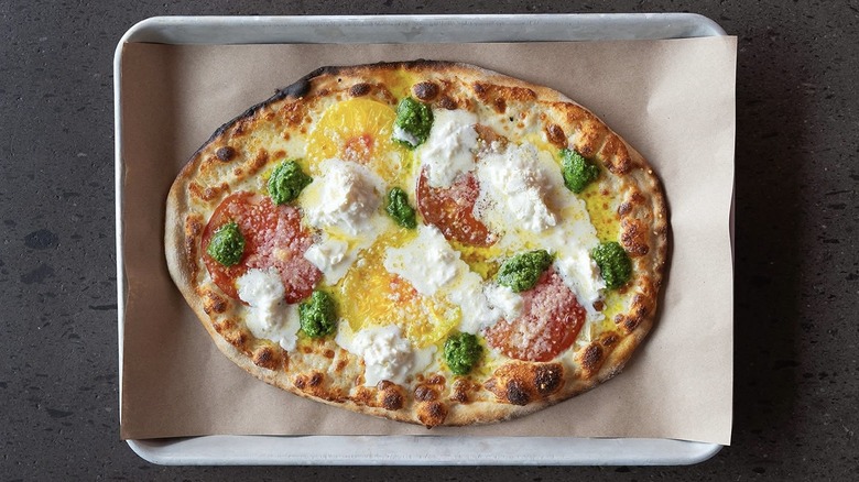 An oval-shaped pizza from Lala's topped with tomatoes, pesto, and white cheese