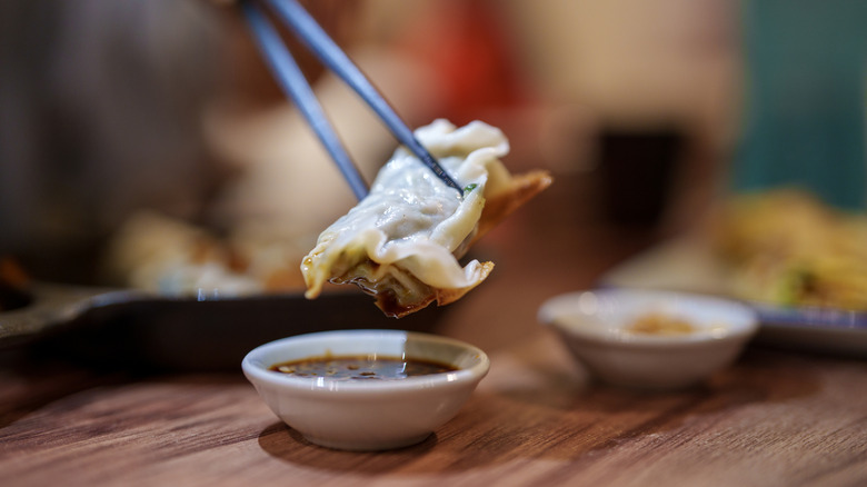 Person dipping dumpling into sauce with chopsticks