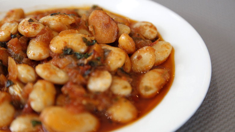 A white bowl with giant beans in tomato sauce