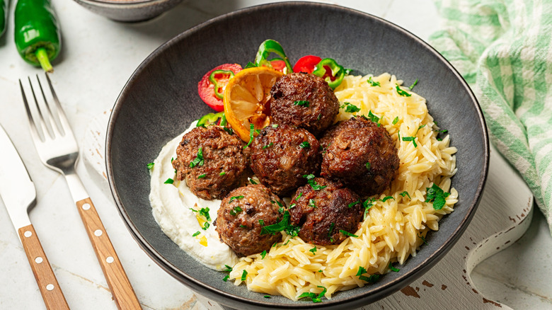 A dark bowl with orzo, keftedes, and a spread