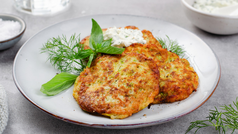 A white plate with three zucchini fritters garnished with herbs