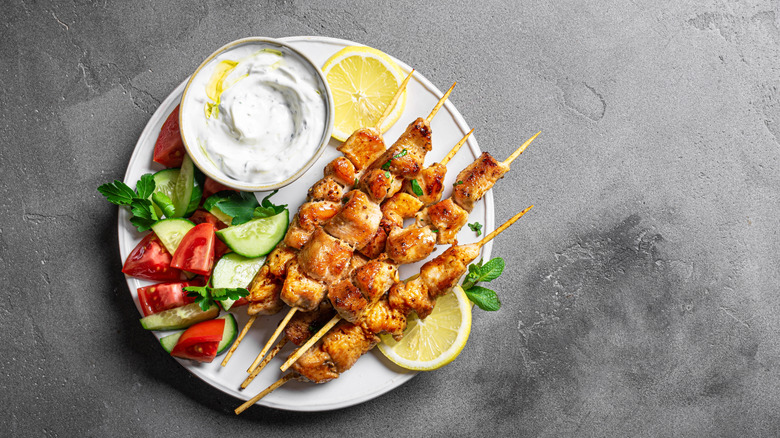 Chicken souvlaki skewers arranged on a pate with veg and sauce