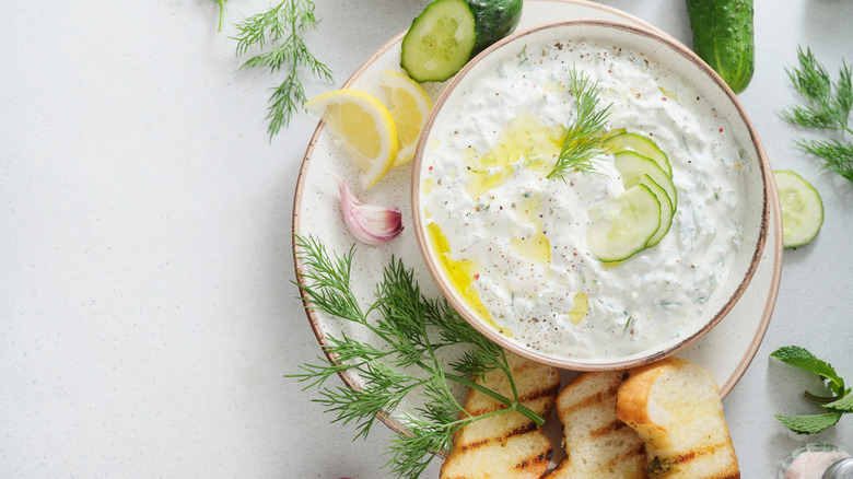 A bowl of tzatziki garnished with pepper, dill, and sliced cucumbers