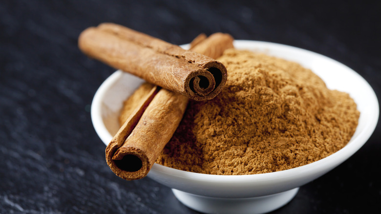 Bowl of cinnamon with cinnamon sticks on black table