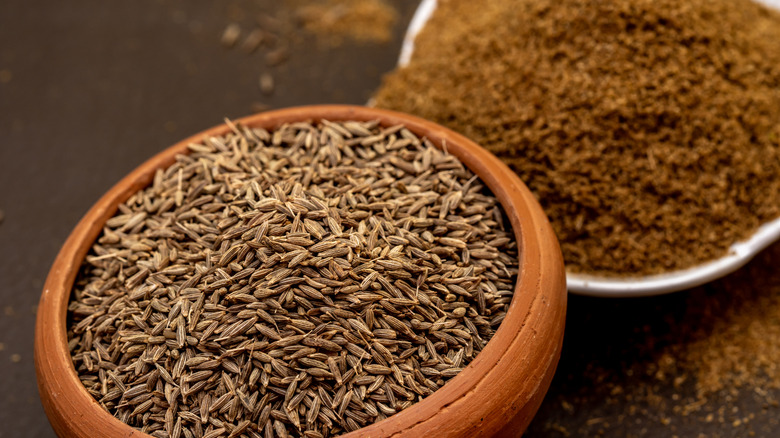Bowl of cumin seeds with ground cumin beside it