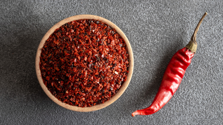 Whole chili and bowl of chili pepper flakes against gray background