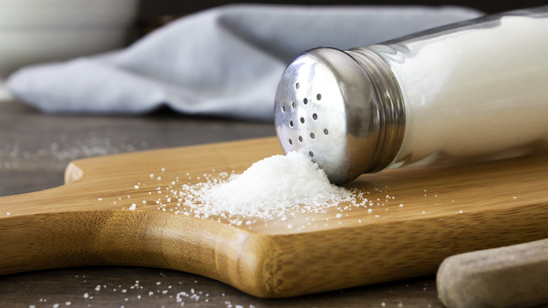 Salt shaker spilling onto wooden cutting board