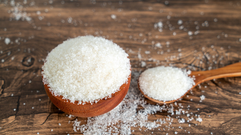 Bowl and spoon filled with sugar on wooden table