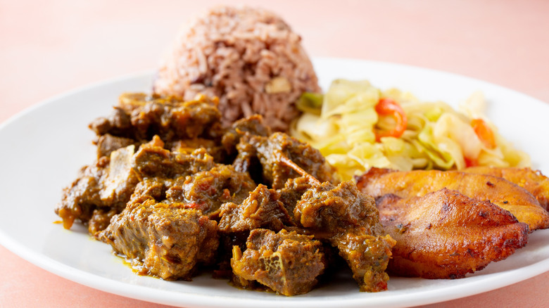 A plate of curry goat with plantains, rice and peas, and salad