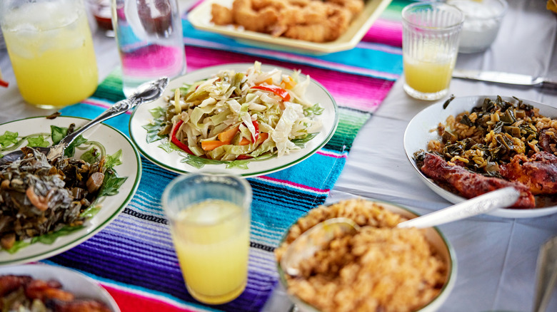 A colorful tablecloth with several Jamaican dishes and drinks spread out