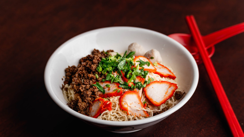 A bowl of kolo mee with chopsticks and a spoon.