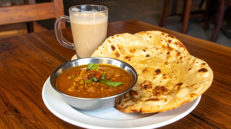 A plate of roti canai with curry and a glass of teh tarik.