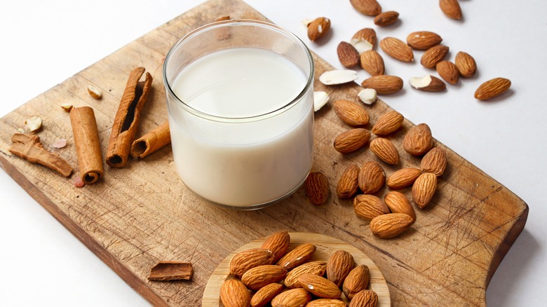 A glass of almond milk on a wooden cutting board surrounded by almonds