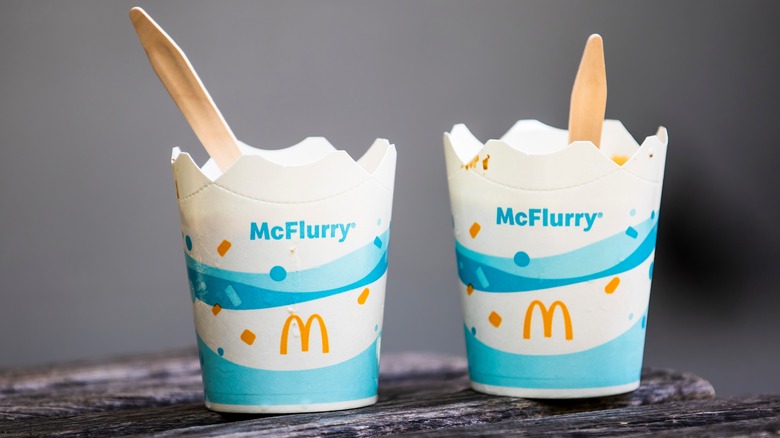 Two McDonald's McFlurrys with spoons in them sitting side by side on a wooden surface