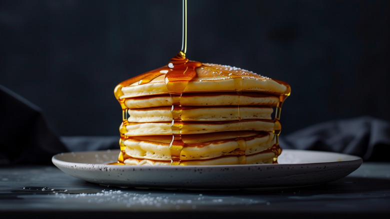 Maple syrup being poured on a stack of pancakes
