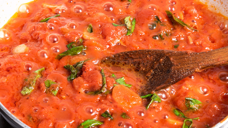 A pan of marinara sauce cooking with a wooden spoon