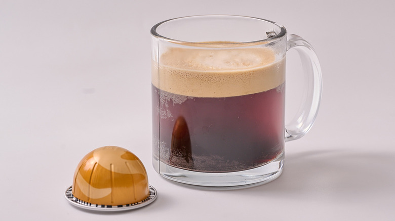 Golden Caramel Nespresso pod and glass of coffee on white table