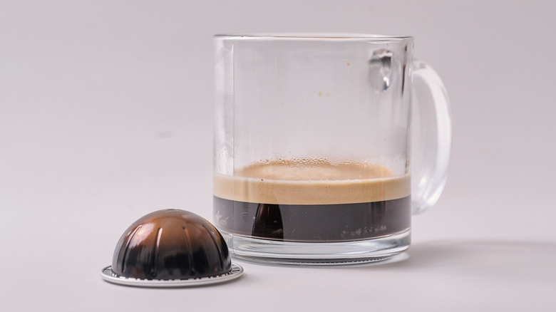 Double Espresso Scuro Nespresso pod and glass of coffee on white table