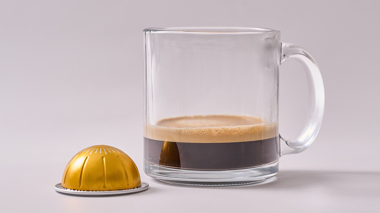 Active Nespresso pod and glass of coffee on white table