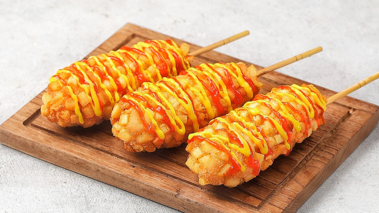 Three Korean gamja hot dogs on a wooden cutting board