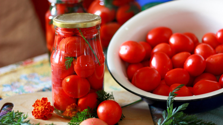 canned tomatoes in a jar next to fresh tomatoes
