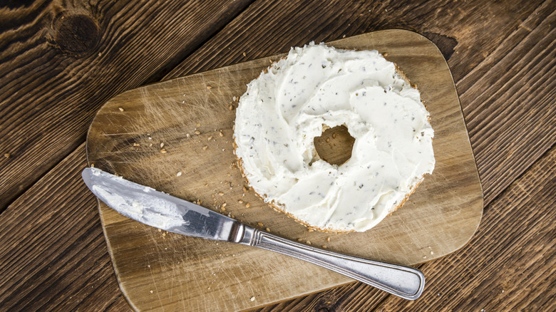 Bagel with herby cream cheese on a wooden surface