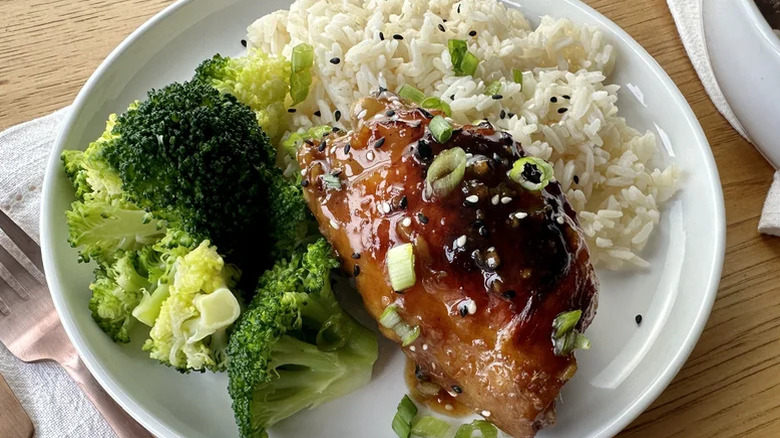 White plate with honey soy marinated baked chicken thighs, white rice, and steamed broccoli garnished with chopped green onions