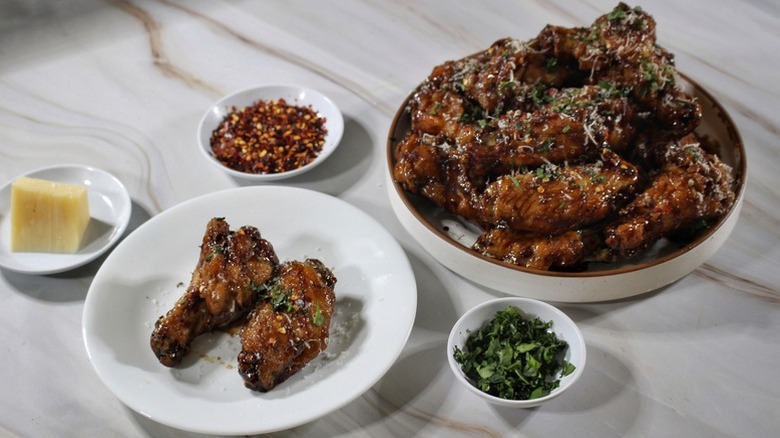 White bowl and plate of balsamic-glazed fried chicken wings garnished with chopped parsley and red pepper flakes