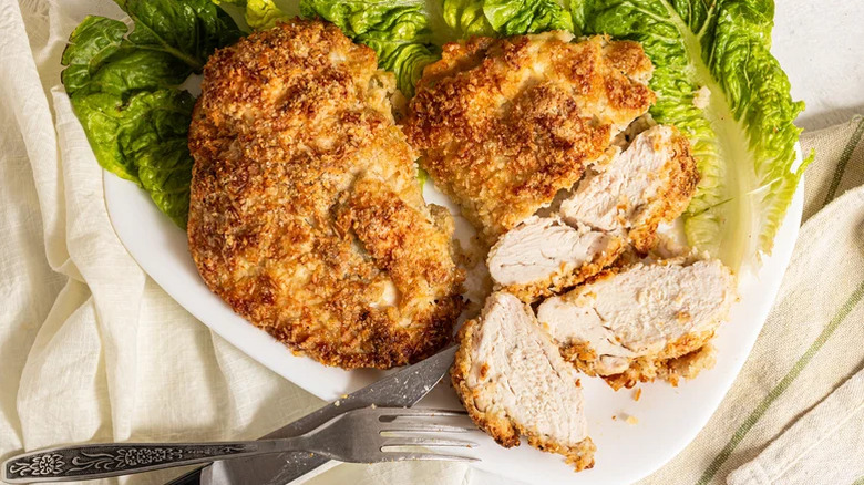 White plate of crispy coconut baked chicken breasts cut into pieces on lettuce leaves
