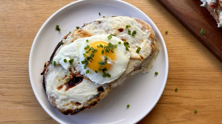 White plate with croque madame on it topped with a fried egg and freshly chopped chives