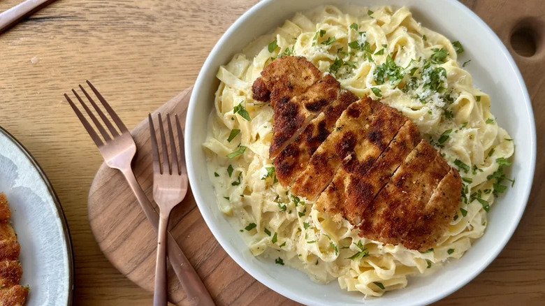 White bowl of creamy fettucine alfredo with sliced breaded chicken breast on top