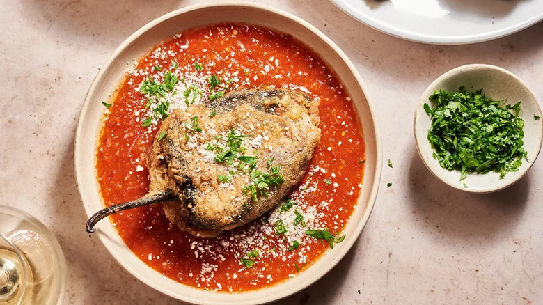 Tan plate of chiles rellenos with guajillo chile sauce garnished with chopped cilantro and queso fresco