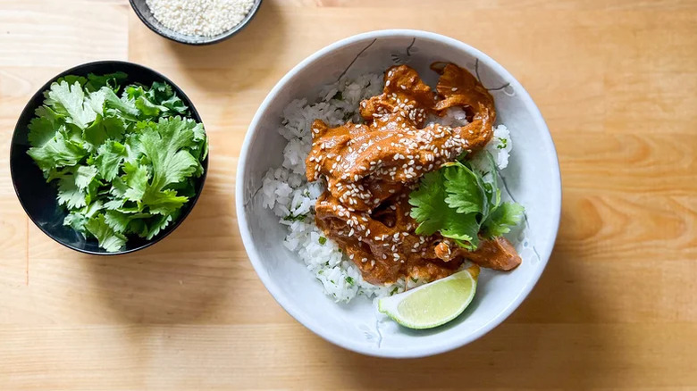 White bowl of chicken mole with white rice and garnished with cilantro leaves and sesame seeds