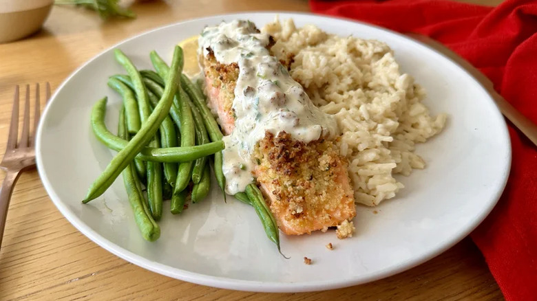 White plate with parmesan crusted salmon covered in remoulade sauce, green beans, and rice