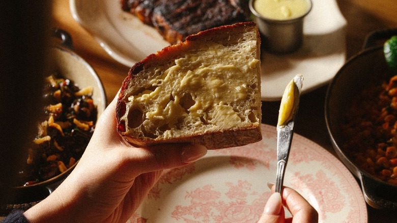 A person buttering a slice of sourdough at Bavette's Bar & Boeuf