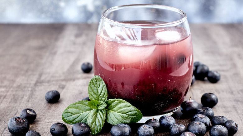 Lemon blueberry muffin-flavored dirty soda in wine glass surrounded by fresh mint and fresh blueberries