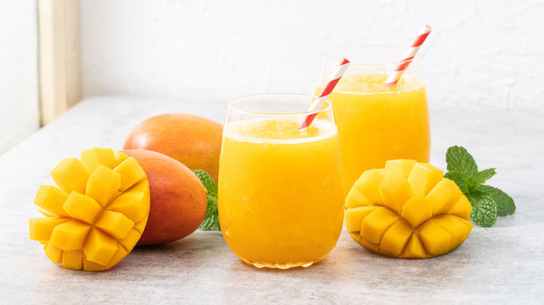 Two glasses of Mango Madness dirty soda surrounded by fresh mangoes