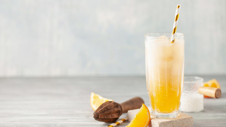 Orange creamsicle dirty soda in a tall glass with a straw