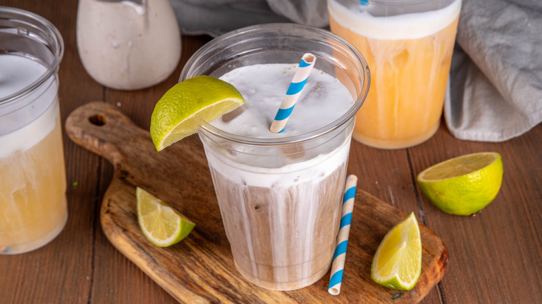 Peanut butter cup dirty soda in plastic glass garnished with lime and a blue and white striped straw