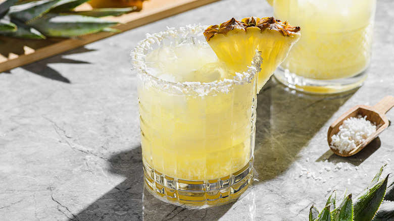 Piña colada dirty soda in a glass garnished with coconut shavings and fresh pineapple slice