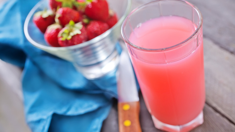 Shirley Temple-flavored dirty soda in a tall glass with fresh strawberries in a bowl behind it