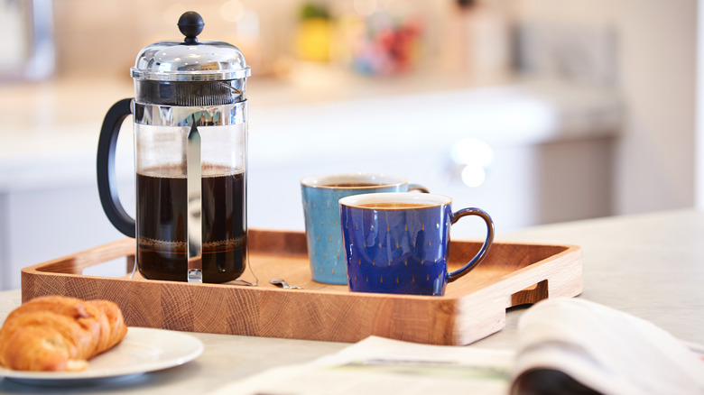 French press and coffee cups on wooden tray